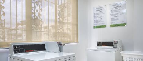 A laundry area with two washing machines, a dryer, and a notice board.