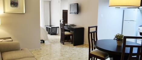 Habitación de hotel con sofá, mesa de comedor con sillas, televisor montado en la pared y refrigerador.
