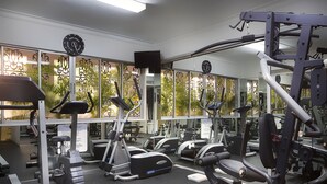 Ein Fitnessstudio mit unterschiedlichen Trainingsgeräten, darunter Laufbänder und Kraftgeräte, und großen Fenstern mit Blick auf Grünflächen.