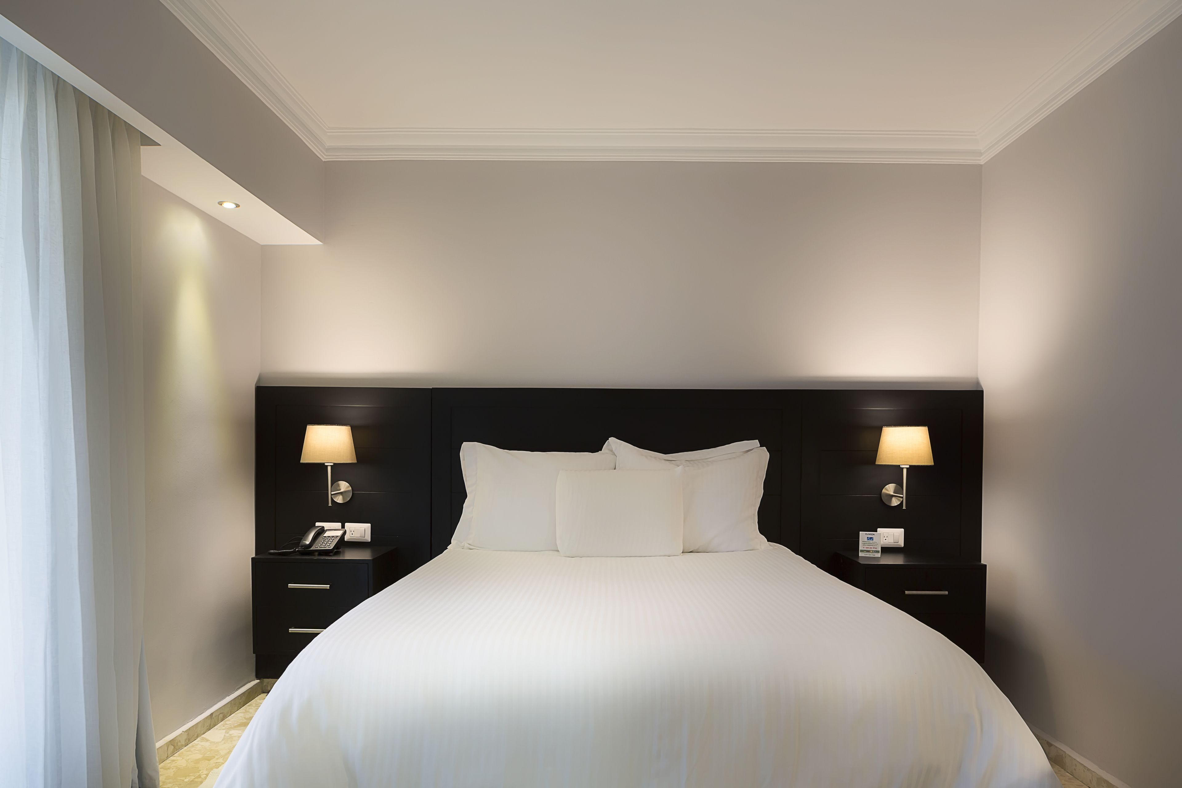 Una habitación de hotel con una cama grande, dos mesitas de noche con lámparas y un cabecero oscuro.