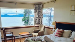 Habitación de hotel con una cama grande, una silla, una mesita y vista a un lago.