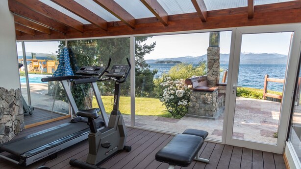 Un espace de remise en forme extérieur abrité, équipé d’appareils d’exercice, d’un banc et offrant une vue sur un lac et des montagnes.