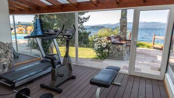 Zona de gimnasio al aire libre techada, con equipo de ejercicio, una banca y vistas a un lago y montañas.