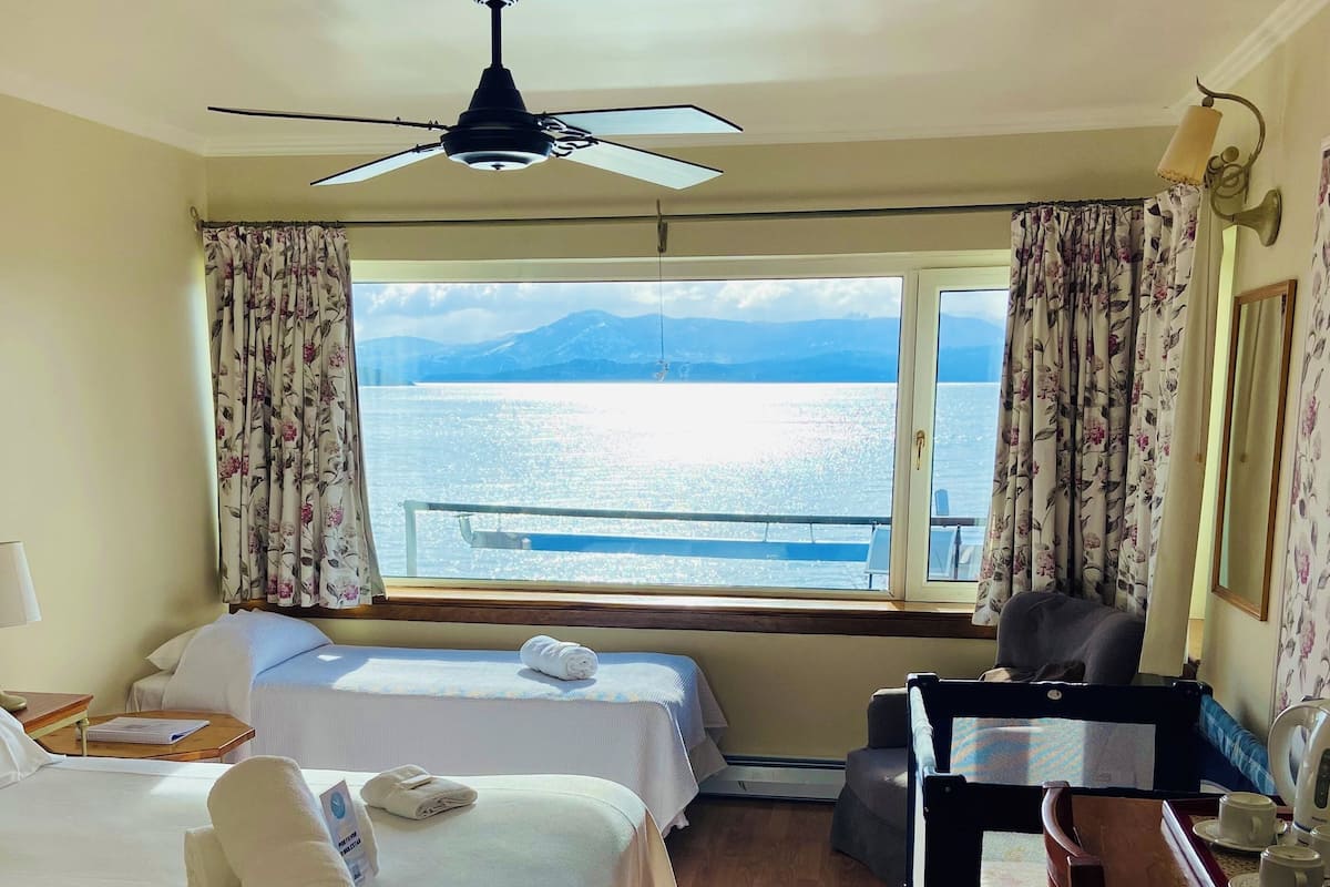 Habitación de hotel con dos camas, un escritorio, una silla, una lámpara de escritorio y vista al mar.