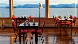 Comedor con vistas a un lago y montañas, con muebles de madera y ventanas amplias.