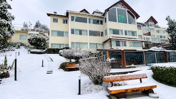 Un hotel de varios pisos con un área exterior cubierta de nieve, que incluye un banco y escalones que conducen a la entrada.