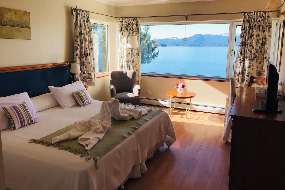 Habitación de hotel con una cama, una silla, una mesita, un televisor y vista a un lago.