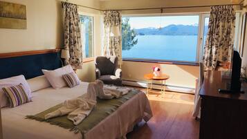 Habitación de hotel con una cama, una silla, una mesita, un televisor y vista a un lago.