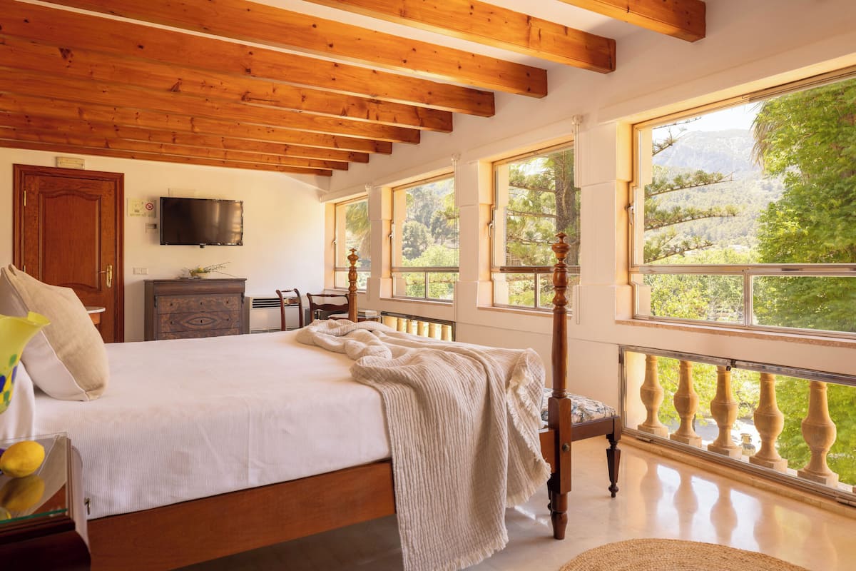 A bedroom with a wooden bed, large windows, and a TV on the wall.