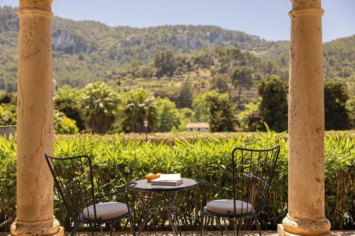 A table with two chairs, a book, and a fruit bowl in a garden with a view of a mountainous landscape.