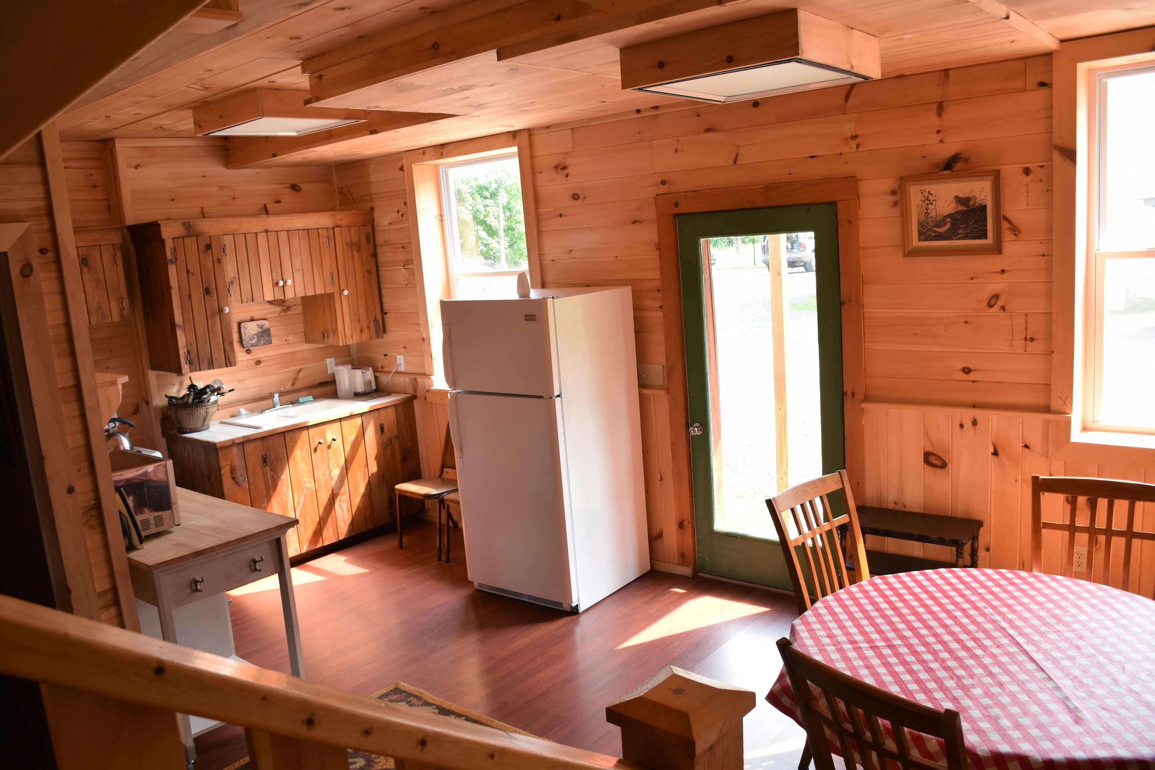 A wooden cabin interior with a kitchen, dining area, and a single window.