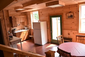 A wooden cabin interior with a kitchen, dining area, and a single window. - Townhouse Hotel (Richfield Springs)