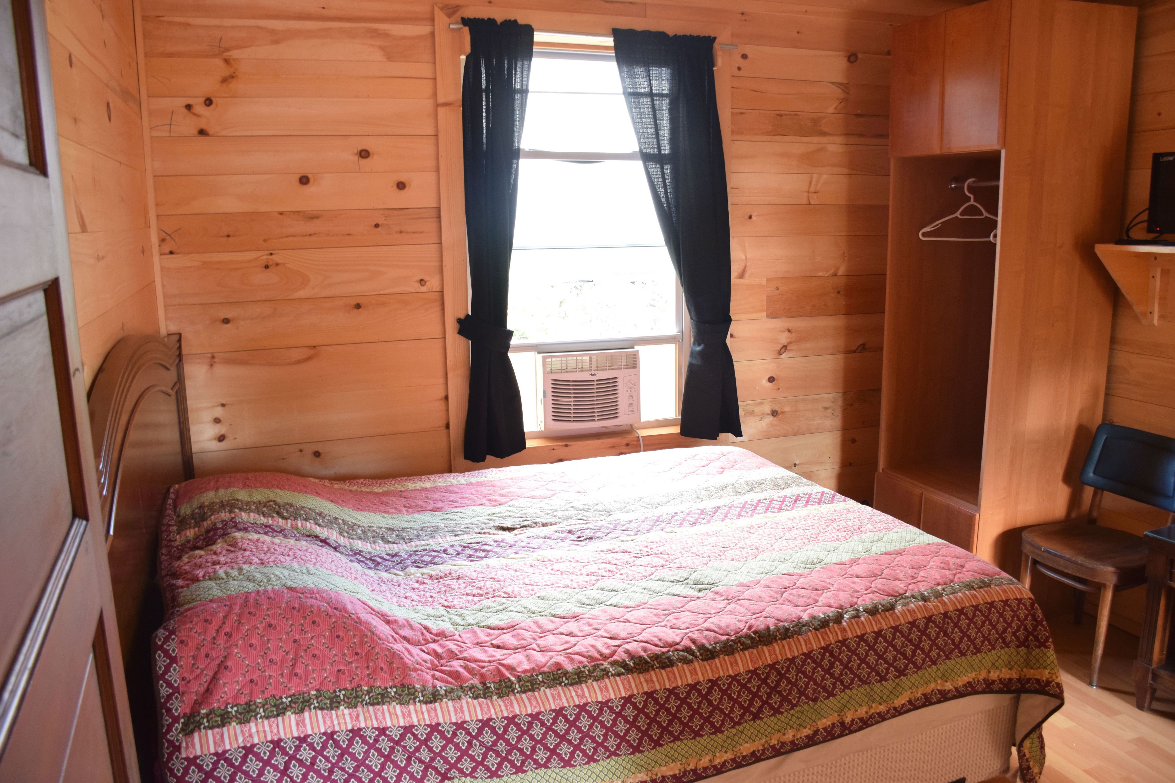 Una habitación con paneles de madera, una cama, una silla y un perchero.