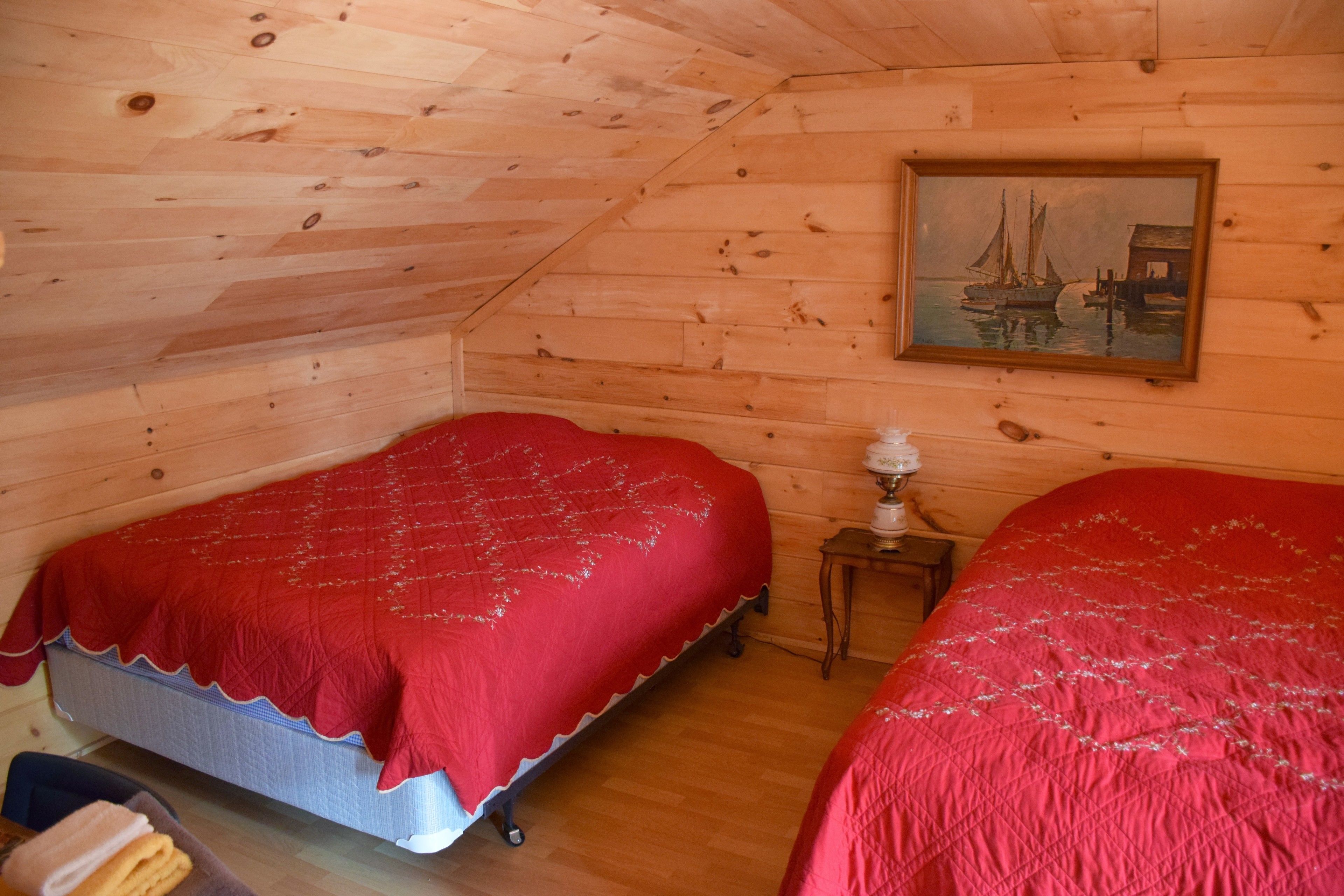 Un dormitorio acogedor tipo cabaña con dos camas, un cuadro en la pared y una pequeña mesa con lámpara.