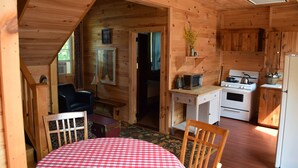 Interior acollidor d'una cabana, amb zona de menjador, cuina i parets de fusta.