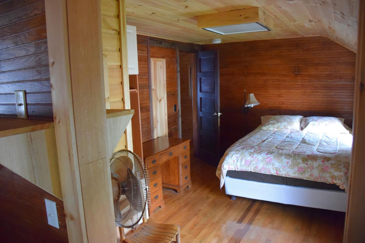 A wooden room with a bed, dresser, and fan.