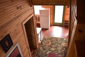 Cozy cabin with a small refrigerator, wooden chair, and patterned rug, featuring a simple design and natural materials.