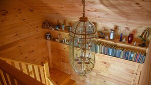Un interior de fusta amb una escala, un llumfer pendent i prestatges amb llibres i objectes decoratius.