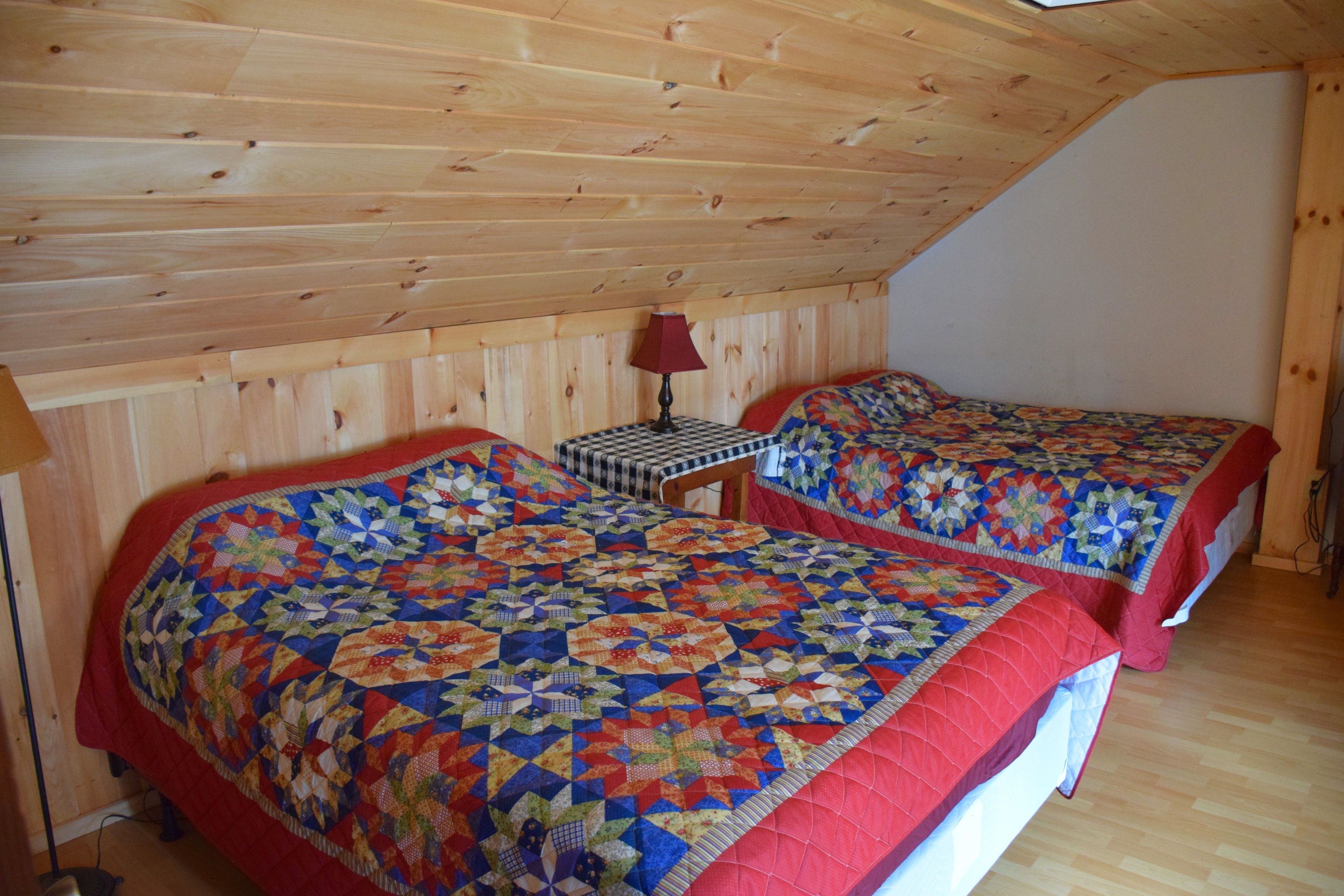 A bedroom with two beds, wooden walls, and a sloped ceiling.