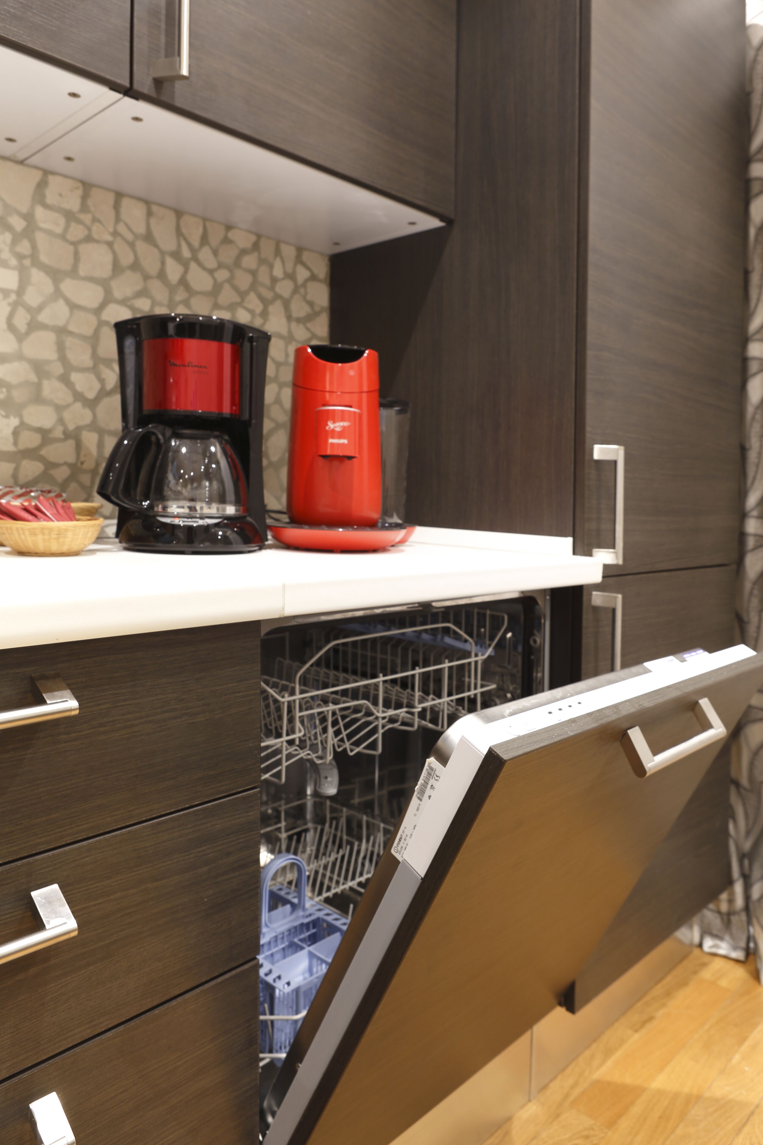 A kitchen with a dishwasher, a coffee maker, and a basket of red cups on the counter.