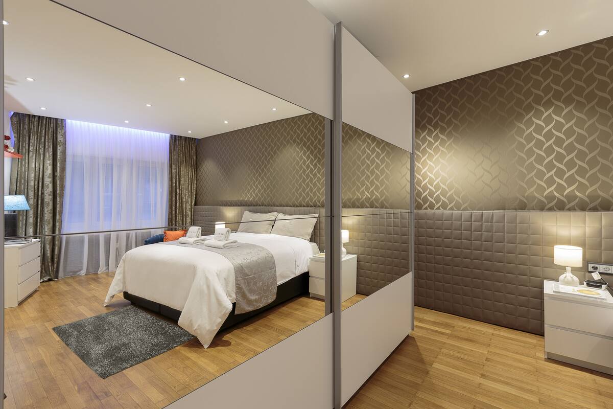Un dormitorio moderno con una cama grande, mesitas de noche, un espejo y una pared con diseño.