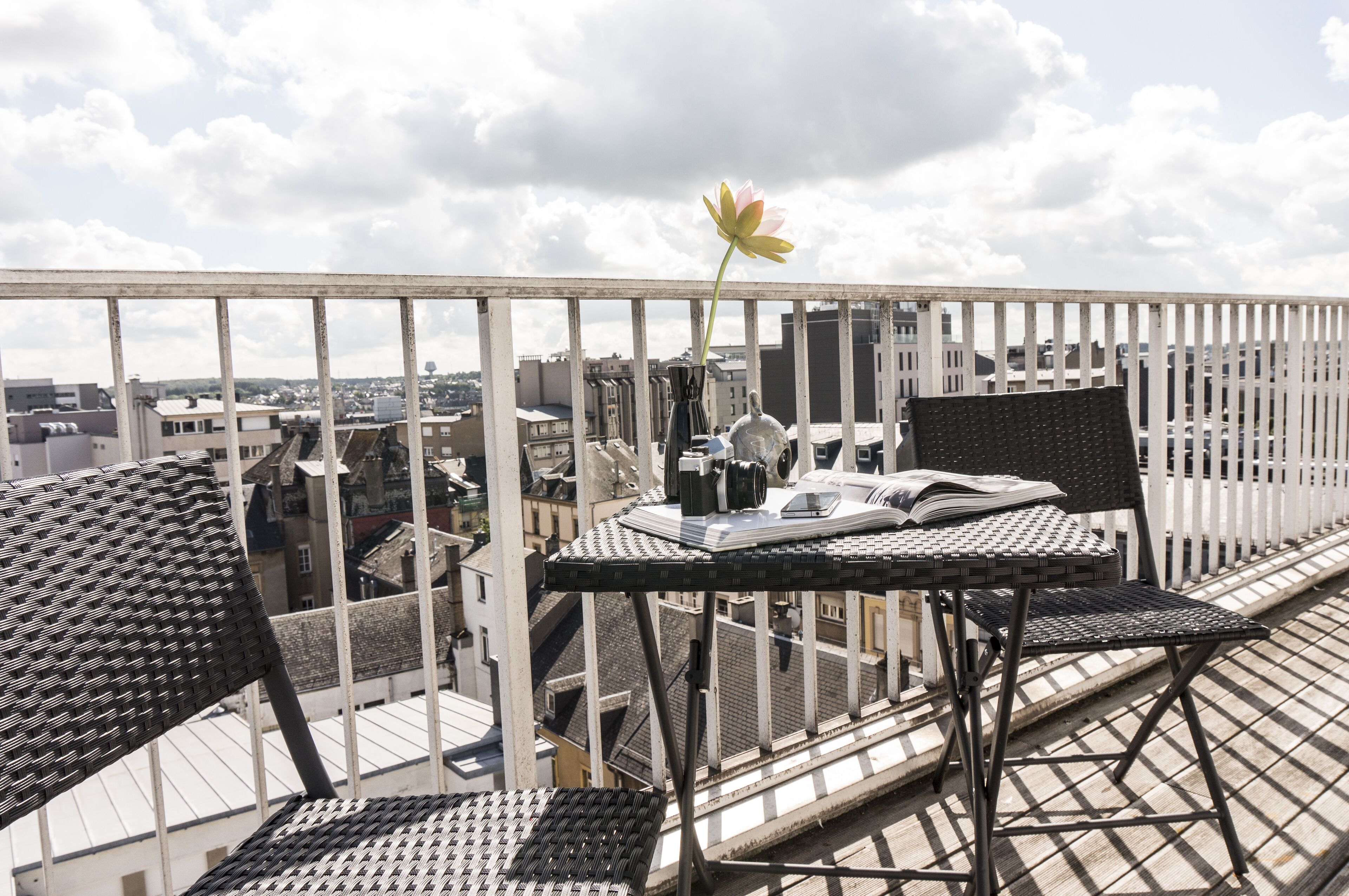Un balcon avec une table et des chaises, une plante en pot et une vue sur la ville.