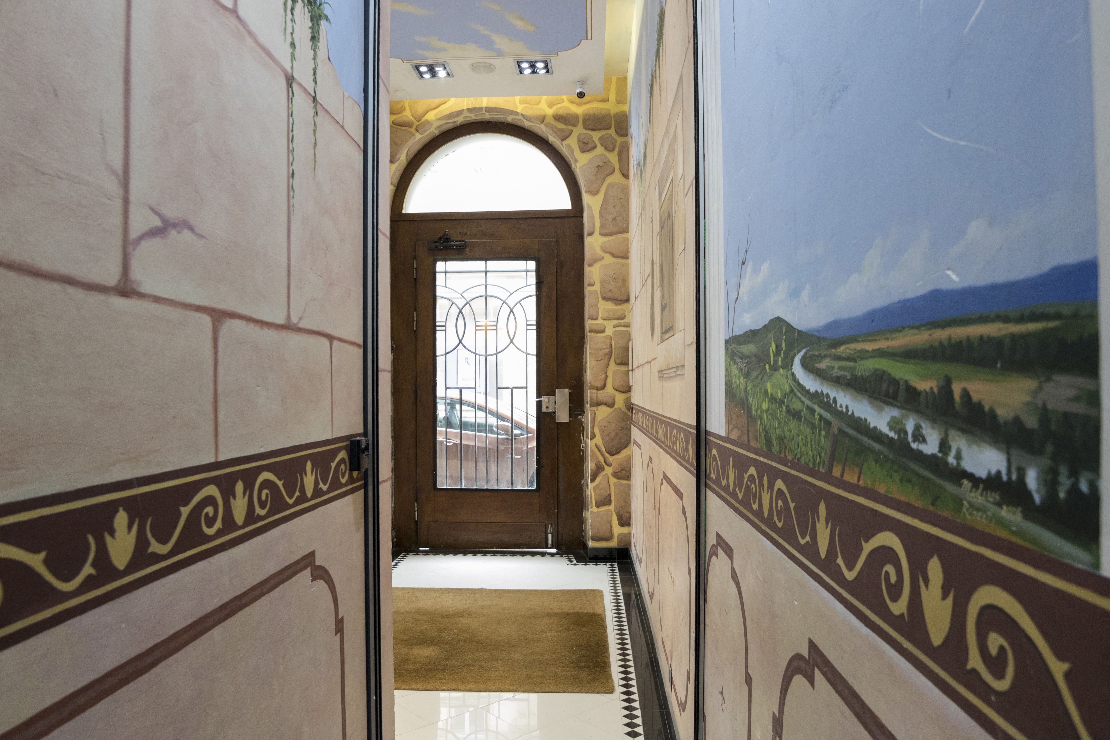 Un couloir avec un mur en pierre, une porte en bois dotée d’un panneau de verre et, sur le mur de droite, une fresque représentant un paysage.