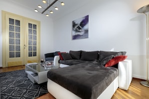 Un salon moderne avec un canapé d’angle, une table basse en verre et un tableau accroché au mur.