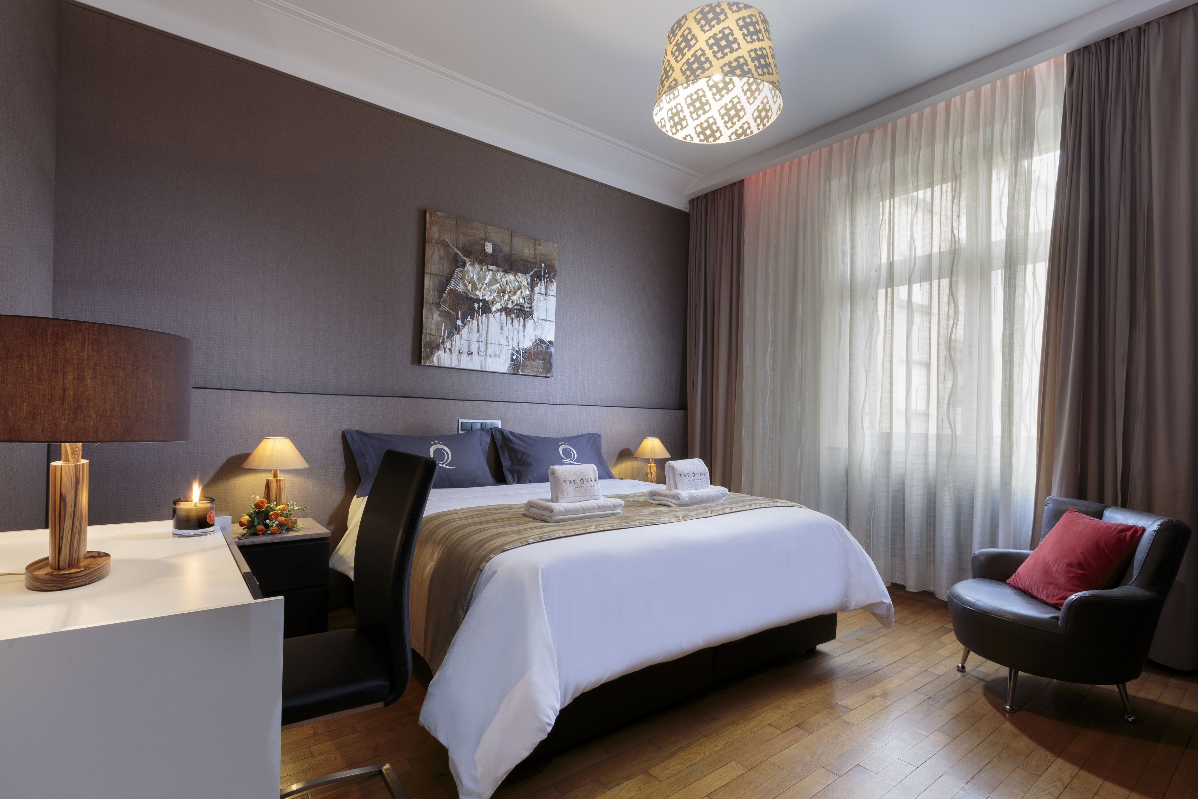 Une chambre d’hôtel avec un grand lit, deux tables de chevet avec des lampes, une chaise, un bureau et une grande fenêtre avec des rideaux.