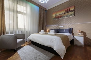 Une chambre d’hôtel avec un grand lit, une table de chevet avec une lampe, une chaise et un tableau au mur.