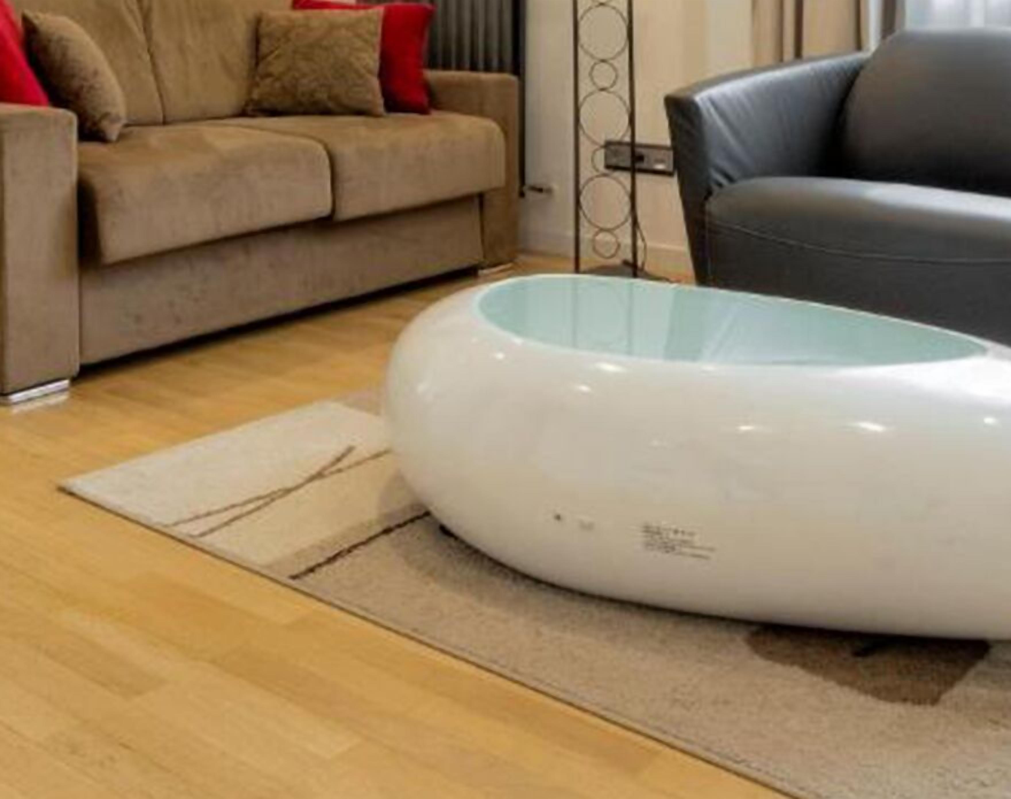Un salon moderne avec un canapé beige, un fauteuil en cuir noir et une table basse ronde en verre, de couleur blanche.