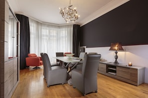 Un salon moderne avec un coin repas, agrémenté d’un lustre, d’une lampe et offrant une vue sur la ville grâce à de grandes fenêtres.
