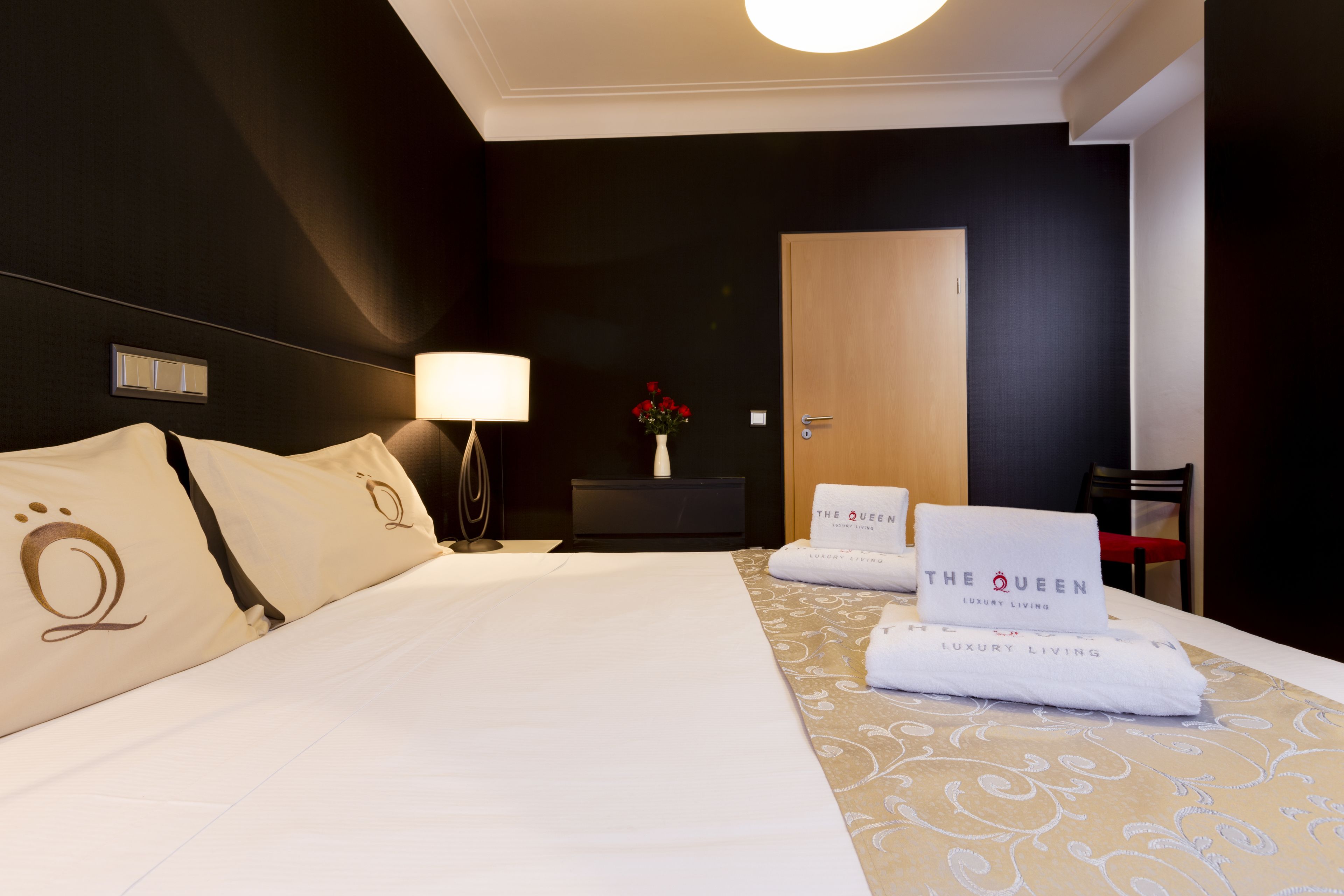 A hotel room with a large bed, a bedside table with a lamp, a vase with flowers, and a door.