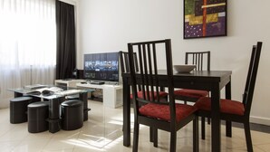 Ein modernes Wohnzimmer mit einem Glastisch, schwarzen Stühlen mit roten Kissen, einem Flachbildfernseher und einer Kaffeemaschine.