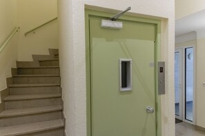 A green door with a window and a keypad lock, a staircase with beige steps, and a handrail.