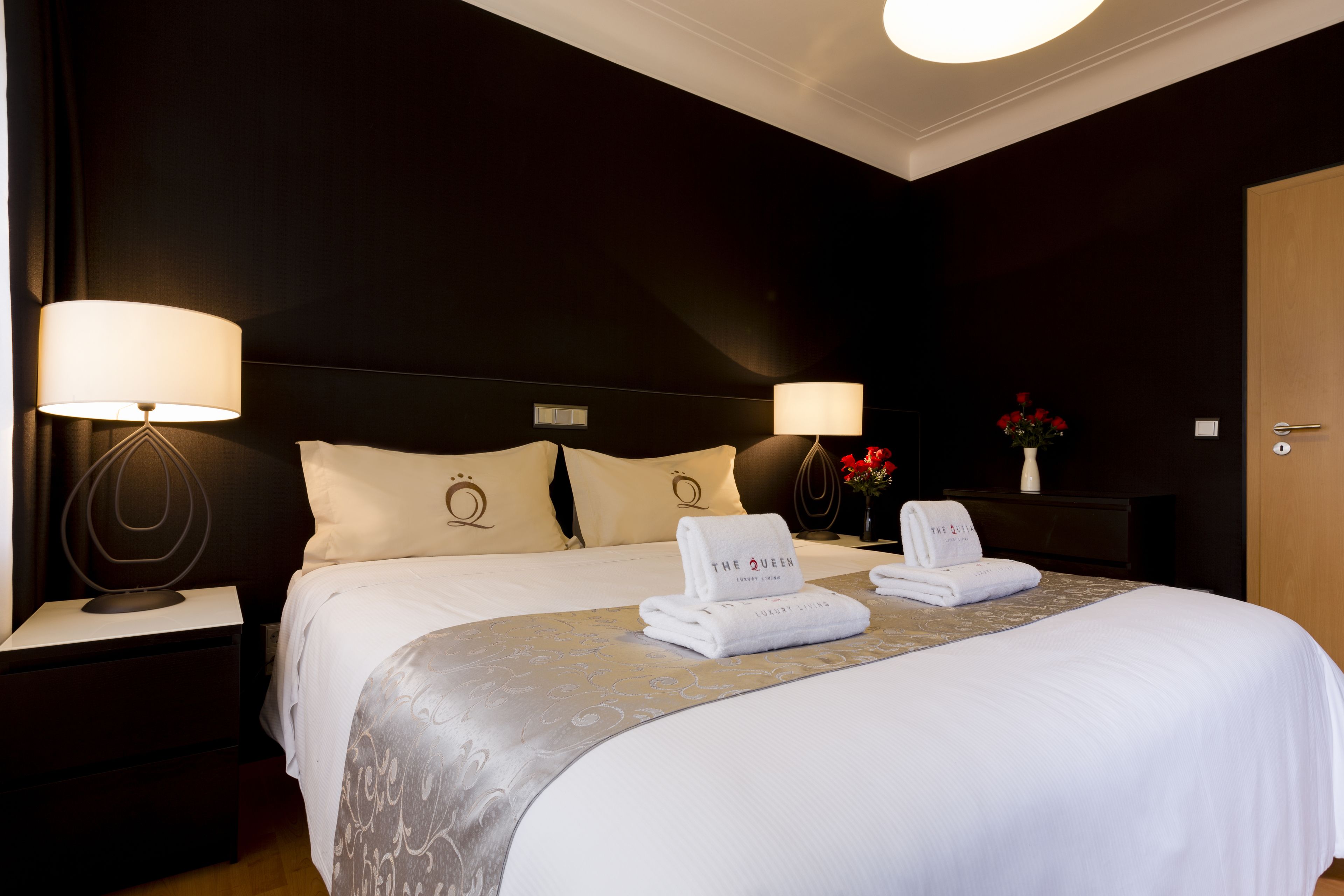 A hotel room with a large bed, two bedside tables with lamps, a nightstand, and a wooden door.