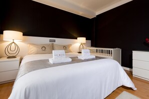 A modern hotel room with a large bed, two bedside tables with lamps, a white dresser, and a radiator.