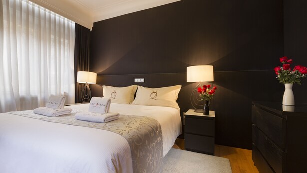 Ein Hotelzimmer mit einem großen Bett, zwei Nachttischen mit Lampen, einem Beistelltisch, einer Kommode und einer Vase mit Blumen.