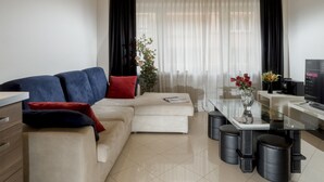 Ein modernes Wohnzimmer mit Sofa, Couchtisch, Fernseher und einer Essecke mit Hockern.