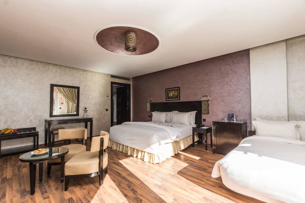 A hotel room with a large bed, two bedside tables, a chair, a small table with a plate of food, and a mirror on the wall.