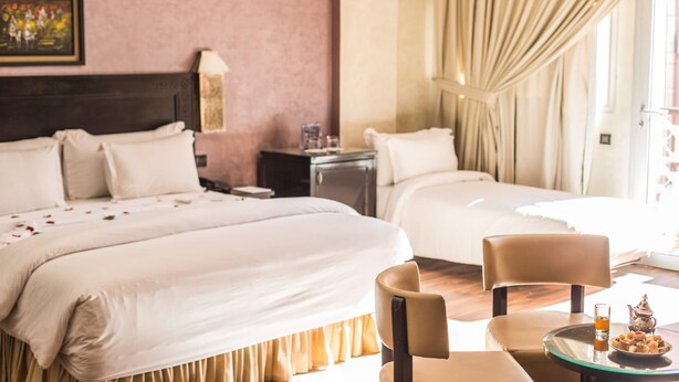 Een hotelkamer met twee bedden, een nachtkastje, een stoel en een tafel met theepot en glazen.