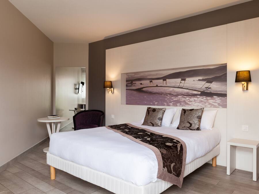 A modern bedroom with a large bed, a headboard with a painting, two bedside lamps, and a small table.