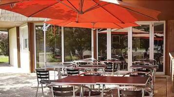 Un espace extérieur aménagé en terrasse, avec des tables et des chaises, protégé par un grand parasol rouge.