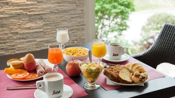 A breakfast table with various food items, a glass of orange juice, a cup of coffee, and a view of greenery outside.