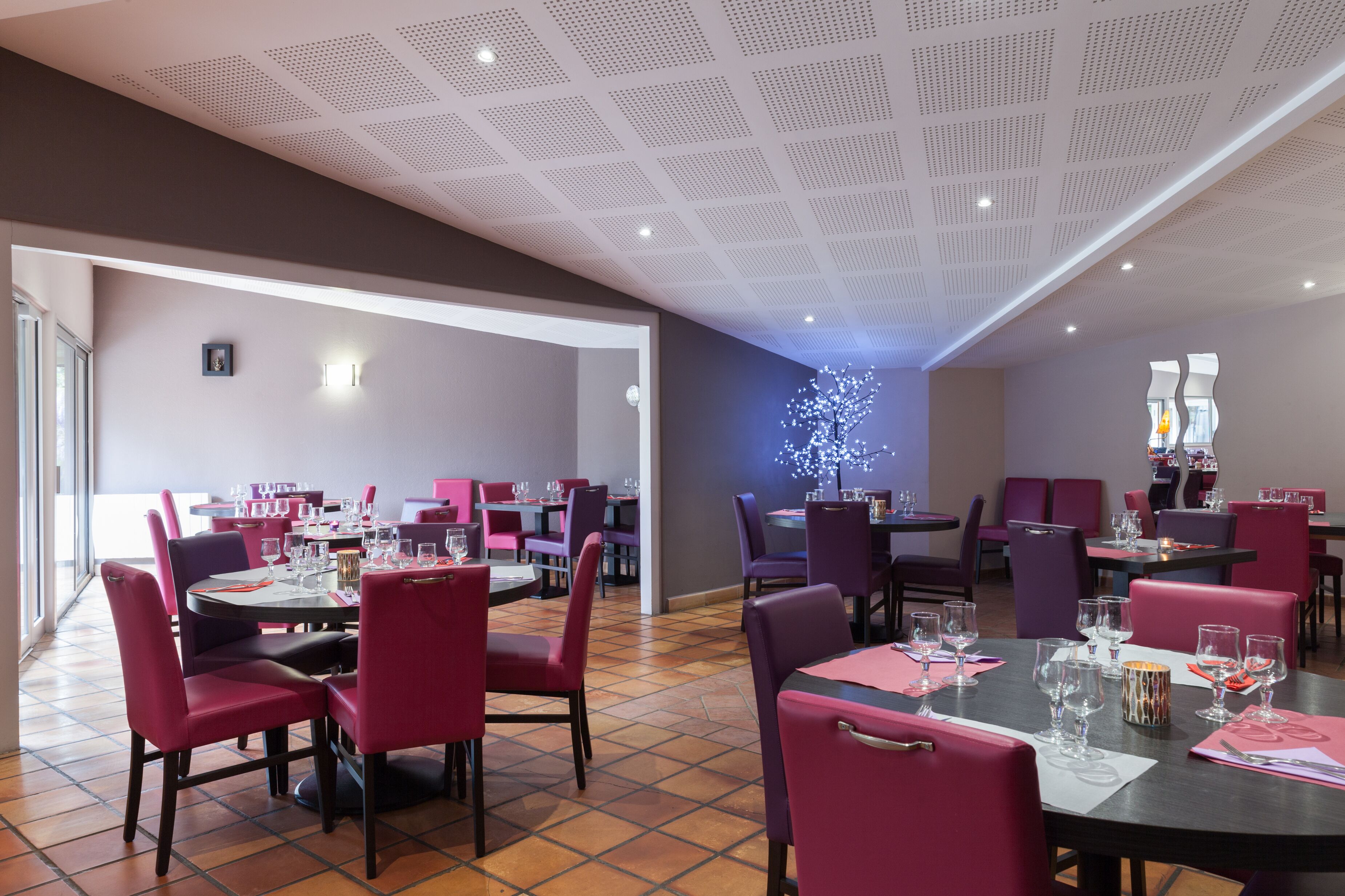 A restaurant with multiple tables and chairs, a ceiling with a grid pattern, and a wall with a decorative light fixture.