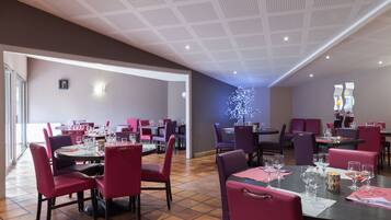 A restaurant with multiple tables and chairs, a ceiling with a grid pattern, and a wall with a decorative light fixture.