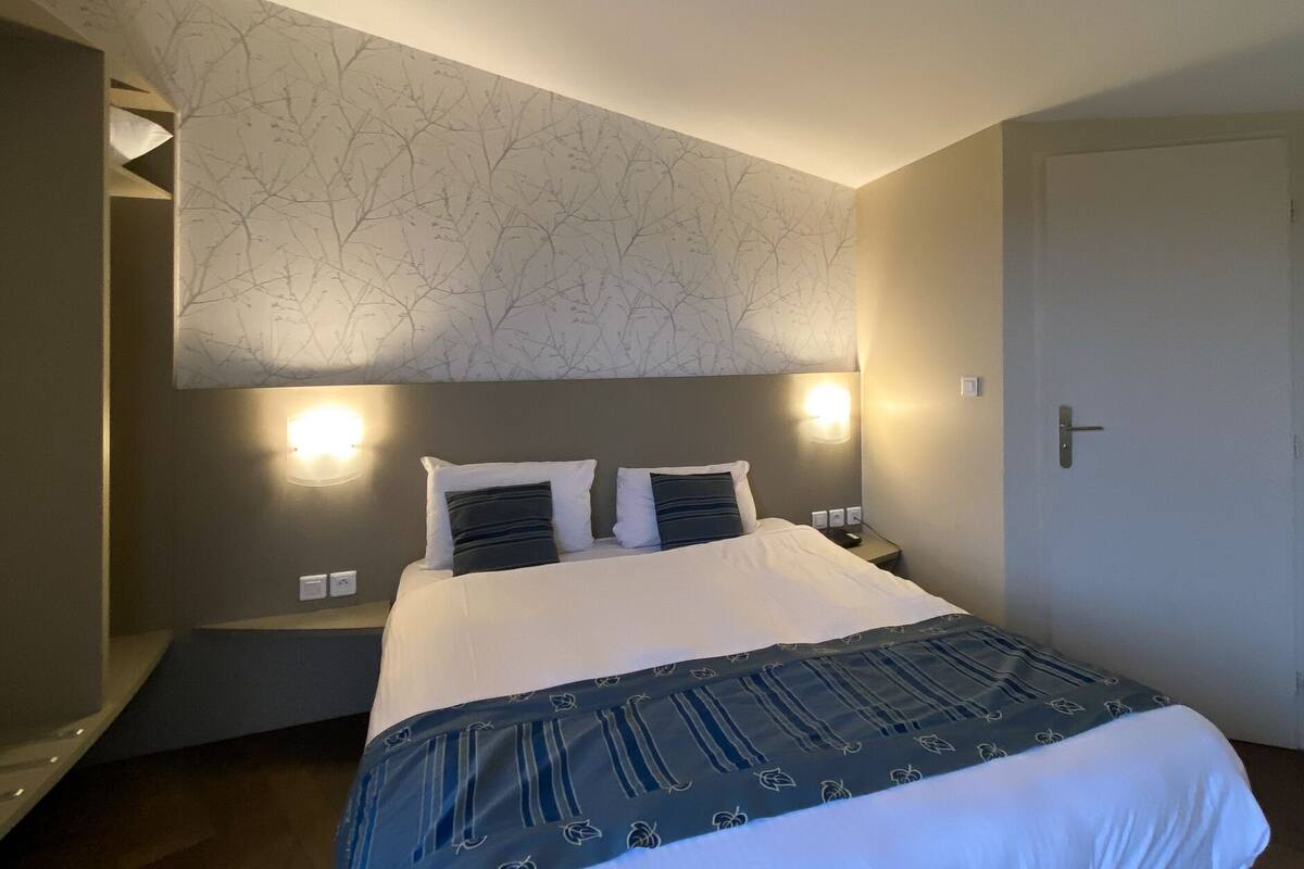 Une chambre d’hôtel avec un grand lit, deux lampes de chevet, un luminaire fixé au mur et une porte.