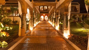 A well-lit pathway leading to a building with arches and columns, surrounded by greenery and plants. - Villa Des Ambassadors (Rabat)
