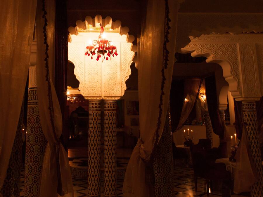 Un interior ornamentado con un candelabro, columnas con motivos y cortinas con drapeado.
