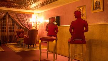 A room with two red bar stools, a chandelier, and a painting on the wall.